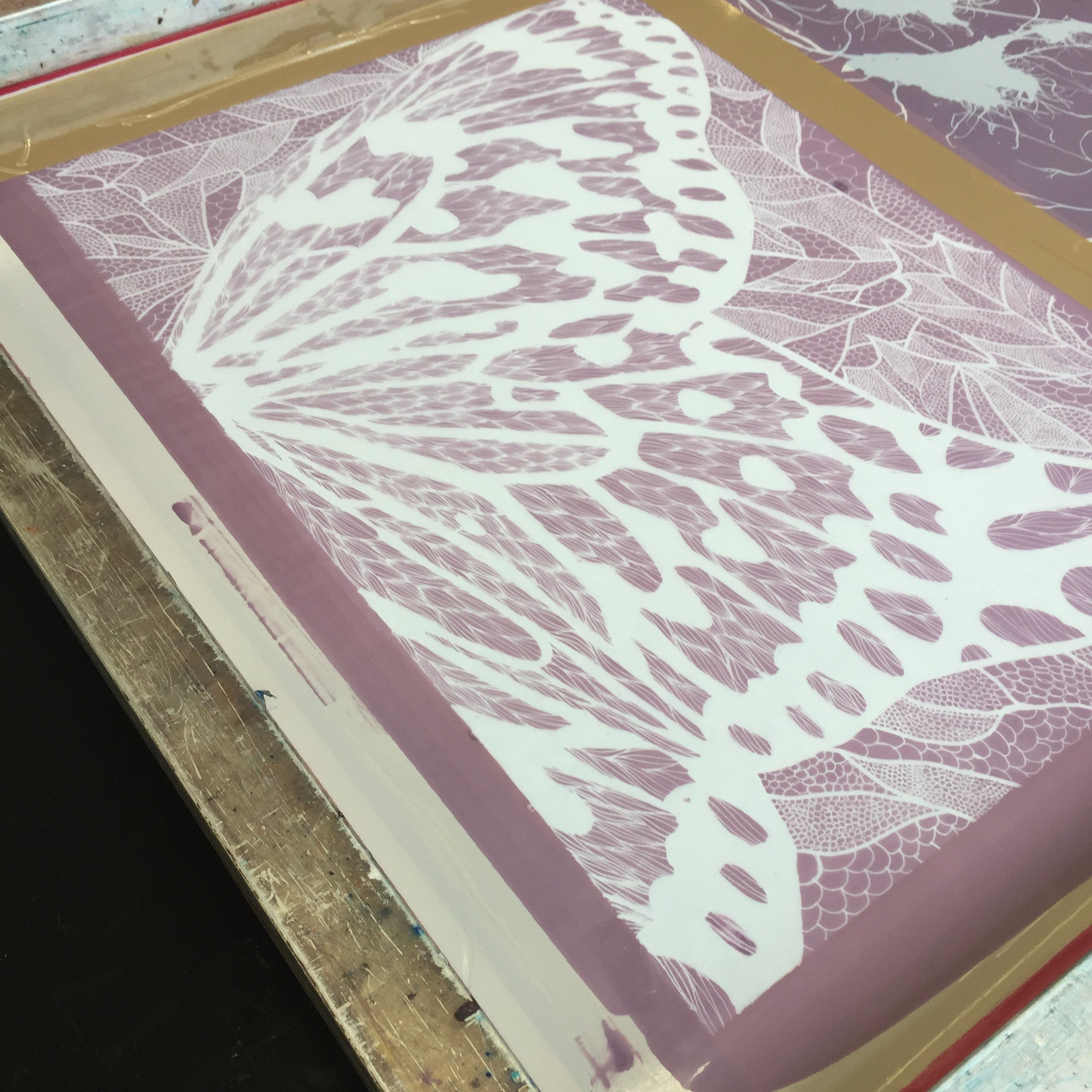 Close-up of a screen printing process with a leaf design on a pink background.