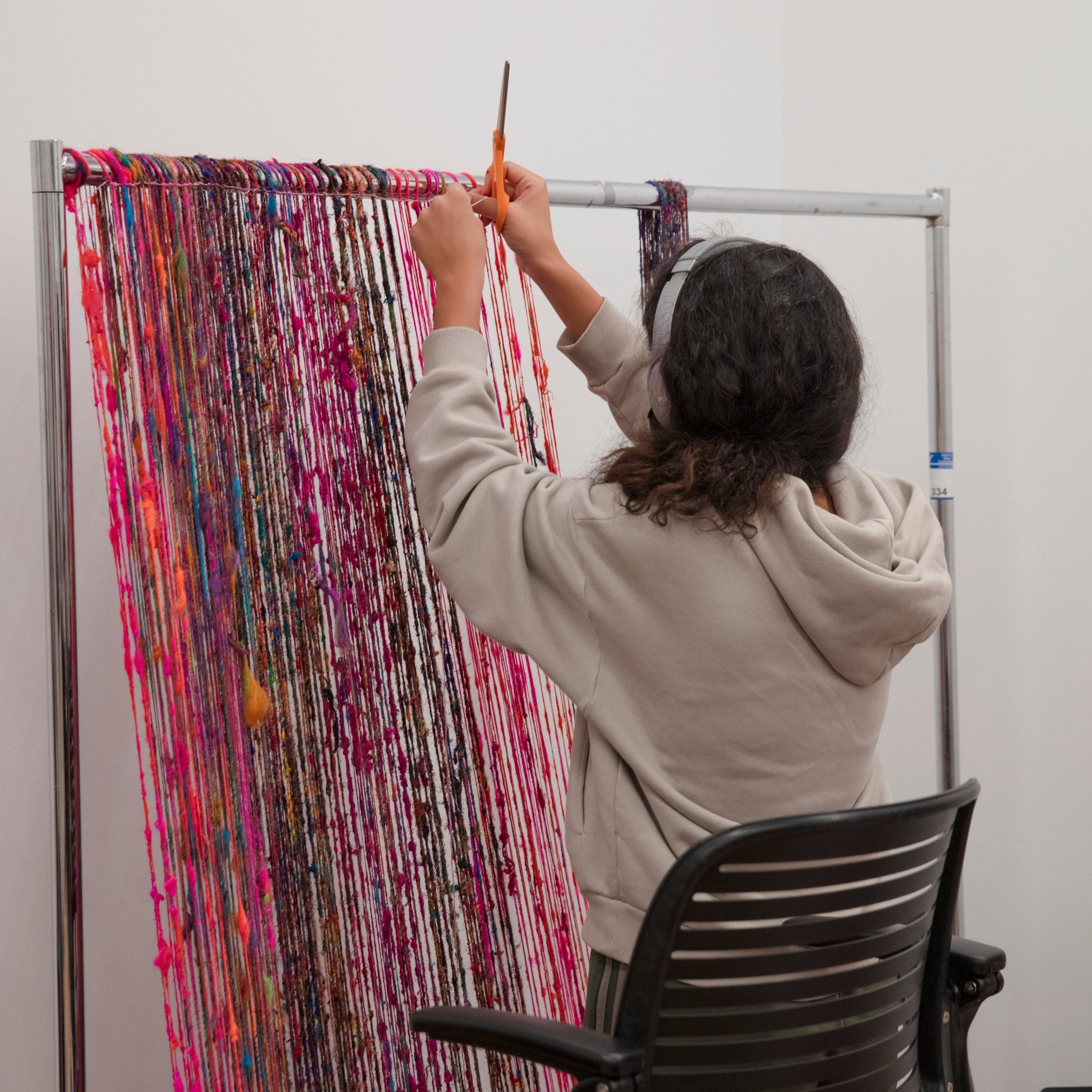 Person working on a colorful art project with yarn in a studio setting.